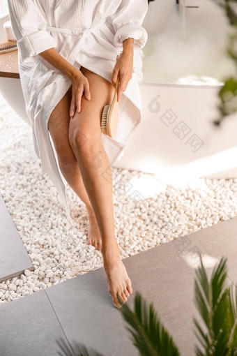 腿年轻的女人光滑的皮肤白色浴袍坐着一边浴缸使皮肤剥浴室