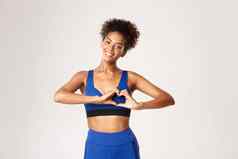 概念体育运动锻炼可爱的非裔美国人适合女运动员显示心手势微笑快乐相机站运动服装白色背景