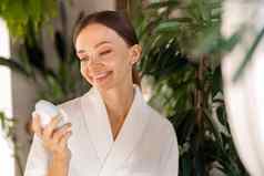 微笑年轻的女人浴袍持有硅胶刷清洗设备敏感的皮肤美例程浴室植物