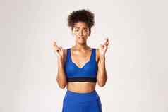 概念体育运动锻炼充满希望的担心非裔美国人女运动员穿蓝色的运动服装咬唇穿越手指好运气使白色背景