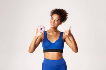 半身照拍摄微笑非裔美国人女运动员蓝色的体育运动装显示竖起大拇指甜甜圈微笑很高兴白色背景