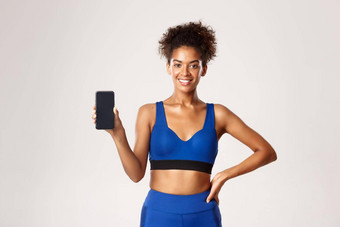 体育运动技术概念快乐运动女人健身服装显示智能手机屏幕微笑很高兴站白色背景