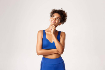 工作室拍摄深思熟虑的有吸引力的非裔美国人健身女人穿蓝色的运动服装<strong>上</strong>左角落里很高兴微笑思考锻炼白色背景