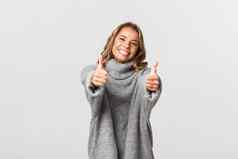 图像快乐美丽的女人灰色毛衣显示竖起大拇指微笑给批准同意赞美好选择站白色背景