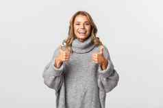 图像快乐满意女人灰色毛衣显示竖起大拇指微笑推荐批准产品站白色背景