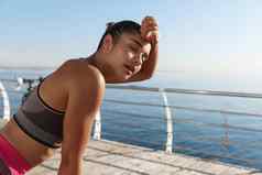 图像美丽的年轻的健身女人气喘吁吁擦拭汗水额头慢跑完成运行锻炼站码头