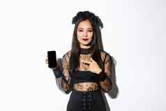 年轻的优雅的女人哥特衣服黑色的花环pointng手指智能手机屏幕很高兴微笑脸站白色背景