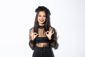 快乐的美丽的亚洲女人女巫衣服显示手势微笑满意批准万圣节服装广告站白色背景