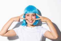 图像可爱的亚洲女人蓝色的假发显示卡哇伊和平手势微笑庆祝万圣节站白色背景