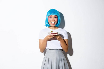 肖像快乐微笑亚洲女孩可爱的化妆穿蓝色的短假发持有一块蛋糕站白色背景