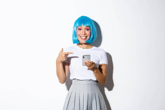 肖像美丽的亚洲女孩穿着动漫字符蓝色的<strong>短假发</strong>指出手指智能手机微笑站白色背景
