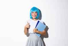图像美丽的微笑亚洲女孩胭脂脸颊穿蓝色的动漫假发持有学校笔记本电脑穿着女学生万圣节聚会，派对显示竖起大拇指批准