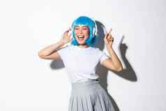 快乐美丽的日本女孩蓝色的假发听音乐耳机跳舞唱歌站白色背景