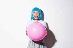 图像快乐的亚洲女孩蓝色的假发庆祝假期穿装万圣节聚会，派对持有大粉红色的气球惊讶
