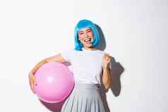 图像赢得快乐的亚洲女孩快乐并庆祝假期穿聚会，派对装蓝色的假发持有大粉红色的气球