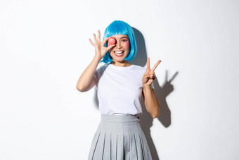 美丽的日本女孩蓝色的假发女学生服装持有macaron显示和平手势微笑站白色背景