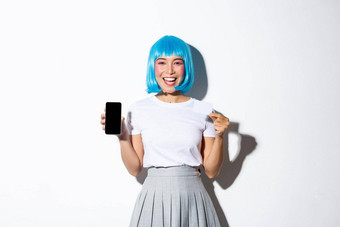 快乐漂亮的亚洲女孩蓝色的短假发聚会，派对化妆持有信贷卡显示智能手机屏幕快乐广告应用程序