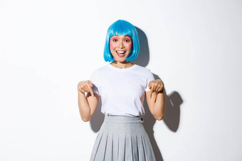 图像快乐愚蠢的亚洲女孩显示标志产品广告指出手指微笑穿蓝色的短假发站白色背景