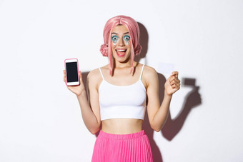 图像兴奋聚会，派对女孩粉红色的假发万圣<strong>节</strong>装显示信贷卡智能<strong>手机</strong>屏幕微笑快乐白色背景