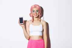 肖像微笑聚会，派对女孩粉红色的假发显示智能手机屏幕满意推荐站白色背景