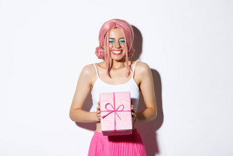 肖像快乐美丽的生日女孩兴奋接收生日礼物微笑快乐站粉红色的假发聚会，派对装白色背景