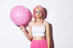 图像年轻的时尚的女孩持有粉红色的气球穿聚会，派对假发庆祝假期站白色背景