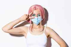 冠状病毒社会距离生活方式概念特写镜头美丽的快乐的女孩医疗面具粉红色的假发住积极的显示和平标志眨眼快乐