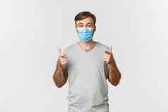 概念流感大流行冠状病毒社会距离兴奋英俊的男人。灰色的t恤医疗面具显示竖起大拇指微笑喜欢好