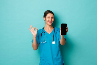 科维德流感大流行医学概念图像微笑美丽的女医生穿实习医生风云显示移动电话屏幕<strong>标志推荐</strong>应用程序蓝色的背景
