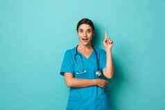 冠状病毒流感大流行社会距离概念图像兴奋女医生穿实习医生风云的想法提高手指尤里卡手势站蓝色的背景