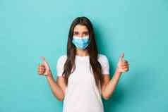 概念流感大流行科维德社会距离自信浅黑肤色的女人女人白色t恤医疗面具显示竖起大拇指批准站蓝色的背景