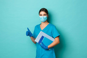 科维德流感大流行医学概念图像惊讶女实习生医疗面具手套实习医生风云持有笔记本电脑显示竖起大拇指蓝色的背景