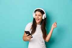 肖像现代漂亮的女孩白色t恤听音乐无线耳机持有移动电话跳舞站蓝色的背景