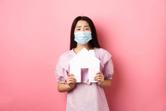 真正的房地产流感大流行概念乞讨亚洲女孩显示纸房子断路穿医疗面具公寓站粉红色的背景