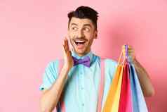 惊讶快乐男人。尖叫快乐标志持有购物袋站粉红色的背景