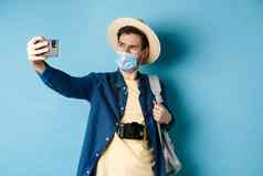 科维德流感大流行旅行概念旅游夏天假期采取自拍医疗面具拍摄智能手机站蓝色的背景