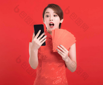 快乐中国人一年惊讶年轻的女人持有<strong>红色</strong>的信封幸运的看移动电话