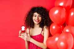 漂亮的高加索人女人订婚了情人节一天女孩收到婚姻建议情人假期显示金环小盒子站心气球红色的背景