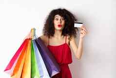 兴奋女人红色的衣服持有购物袋显示塑料信贷卡商店折扣白色背景