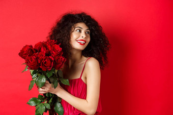 温柔的年轻的女人优雅的红色的衣服持有浪漫的花束红色的玫瑰微笑梦幻思考情人情人节一天工作室背景