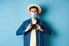 科维德流感大流行旅行概念快乐的旅游夏天他医疗面具采取照片持有相机站蓝色的背景