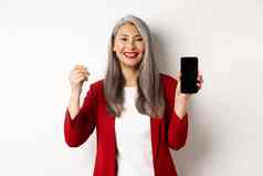 高级亚洲女商人显示塑料信贷卡空白智能手机屏幕微笑相机白色背景