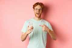 快乐的的家伙会说话的互联网促销微笑惊讶指出手指智能手机站粉红色的背景