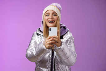 逗乐兴奋有吸引力的金发碧眼的女朋友持有智能手机记录视频的男朋友一步滑雪板时间捕捉记忆移动相机站幸福的紫色的背景