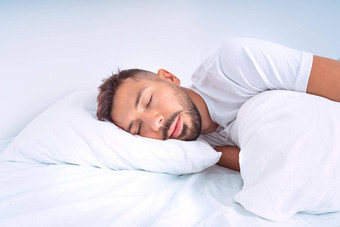 英俊的可爱的男人。睡觉床上白色用品厂男人。说谎枕头享受好健康的睡眠
