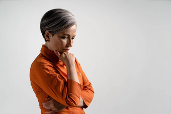 沉思的成熟的灰色头发的女人橙色衬衫漂亮的中期岁的灰色头发的女人橙色衬衫孤立的灰色背景