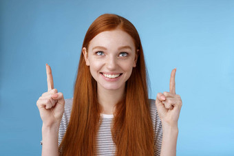 快乐的好奇的逗乐快乐娱乐红色头发的人漂亮的女孩盯着指出微笑批准有趣的产品看的绩效享受很酷的假期广告片站蓝色的背景