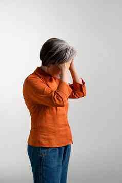 情绪低落的抑郁成熟的灰色头发的女人橙色衬衫持有额头手漂亮的中期岁的灰色头发的女人橙色衬衫孤立的灰色背景