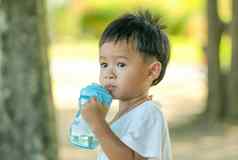 男孩喝水蓝色的瓶绿色花园一天光