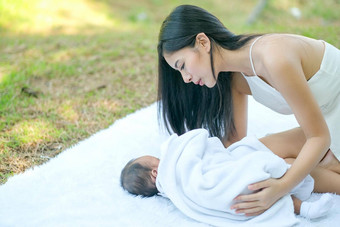 亚洲美丽的妈妈。<strong>护理新生儿</strong>婴儿谎言白色地毯花园